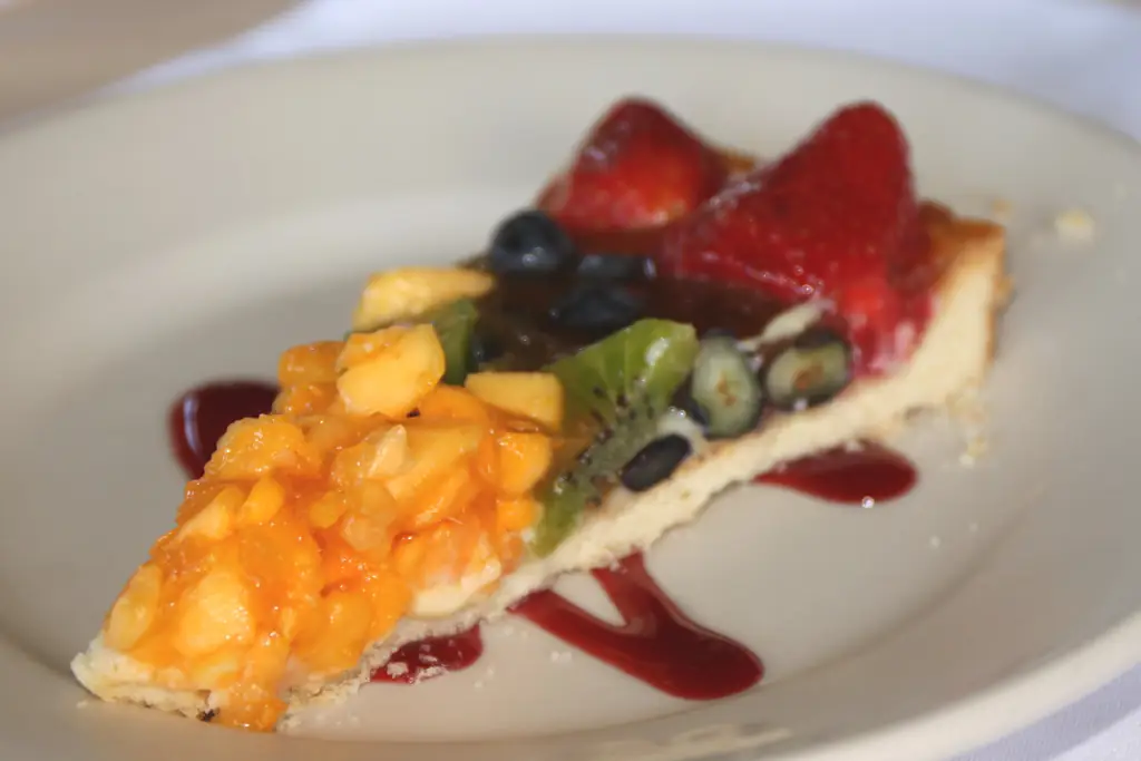 Plated slice of fruit tart with berry sauce